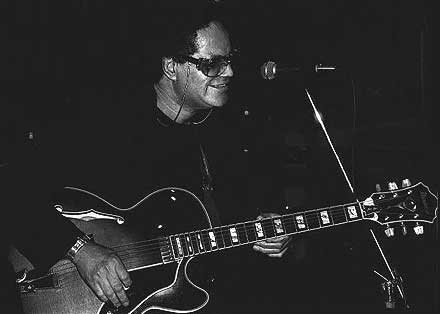 Photo of Sonny Greenwich on-stage, at the microphone, with his guitar